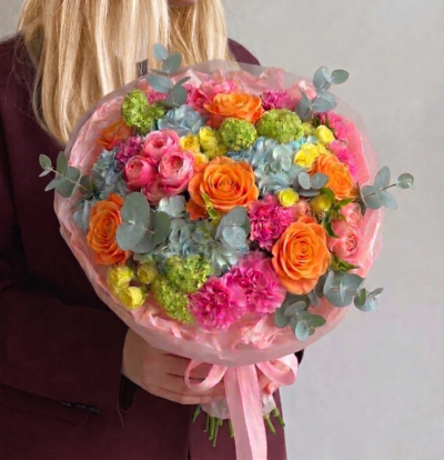 Colourful bouquet with orange roses, pink blooms, blue hydrangea, green accents, and eucalyptus wrapped in blush paper