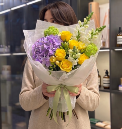 Yellow roses and lavender hydrangea bouquet with green accents wrapped in soft white paper