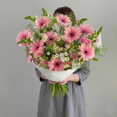 Soft pink and white bouquet with daisy-style blooms, small white flowers, and greenery in a hand-tied arrangement