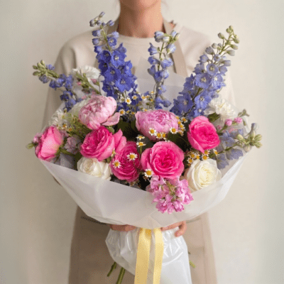 Mother’s Day bouquet with pink roses, blue flowers, and white accents in soft garden-style wrapping