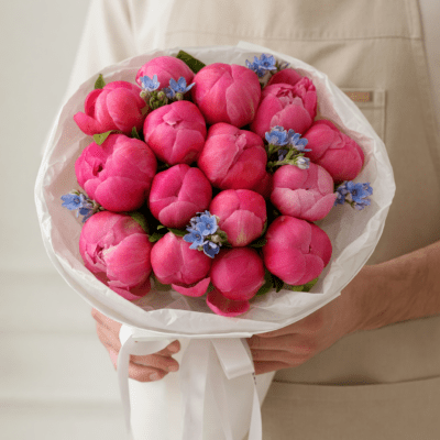 Mother’s Day bouquet with lush pink peonies and small blue accent flowers wrapped in white paper