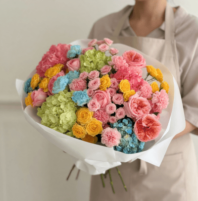 Pastel bouquet with pink roses, yellow flowers, blue and green hydrangea wrapped in white paper