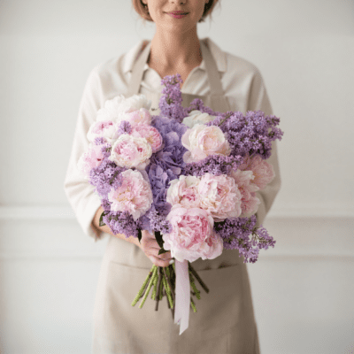 Soft pink and lavender bouquet with large ruffled blooms and delicate purple clusters, hand-tied with ribbon