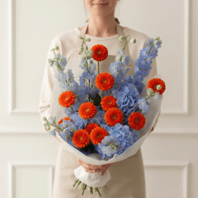 Bouquet with bright orange flowers and soft blue blossoms arranged in a modern, airy style