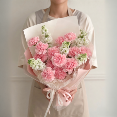 Soft pink carnation bouquet with white accent flowers wrapped in blush and white paper with ribbon