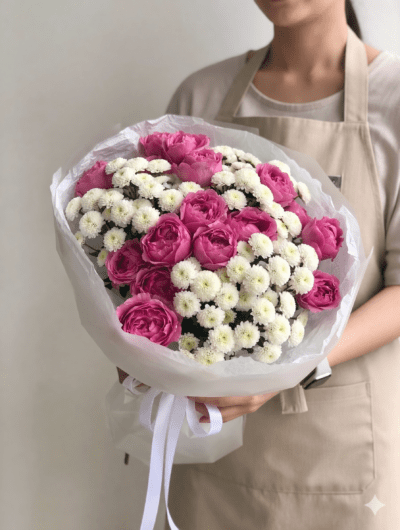 Soft pink garden-style roses with small white flowers wrapped in elegant white paper bouquet held by florist
