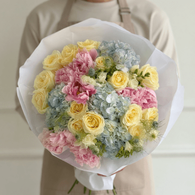 Pastel bouquet with yellow roses, blue hydrangea, and pink flowers wrapped in white paper
