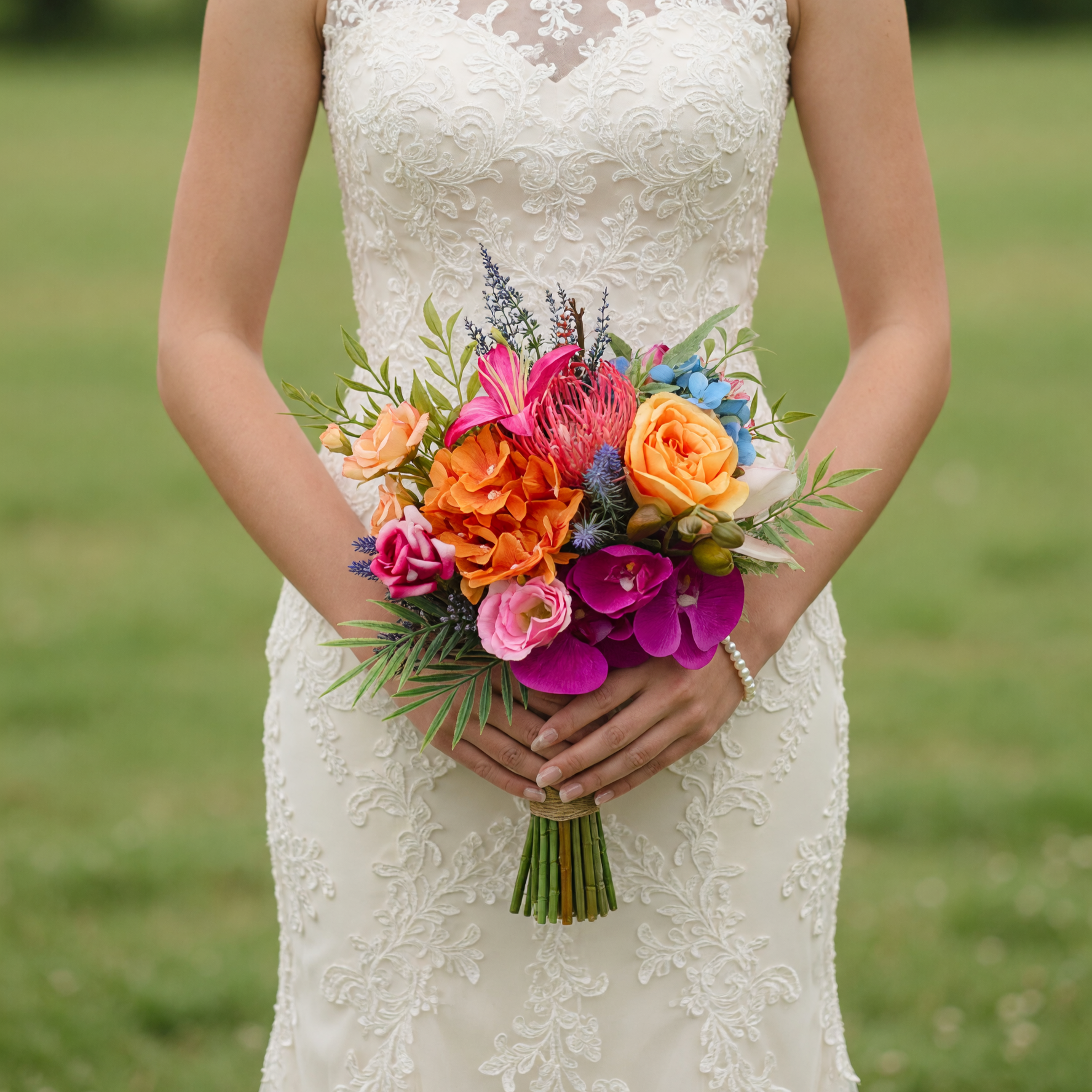 Luxury colorful bridal bouquet with king protea, orange hydrangea, golden roses, magenta orchids, pink lilies, blue hydrangea, eryngium, and fresh greenery for a wedding.