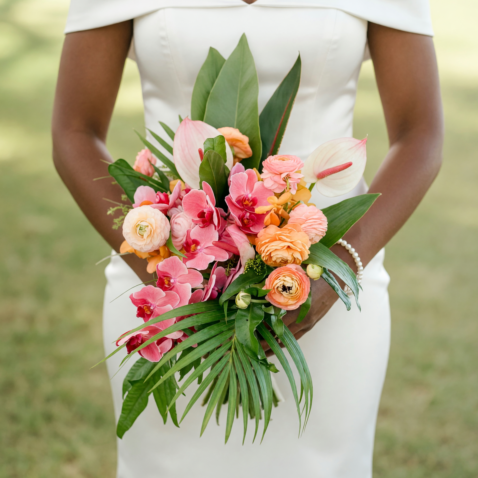 Colorful bridal bouquet with pink orchids, white anthuriums, peach ranunculus, coral flowers, tropical foliage, and palm leaves for an elegant wedding.