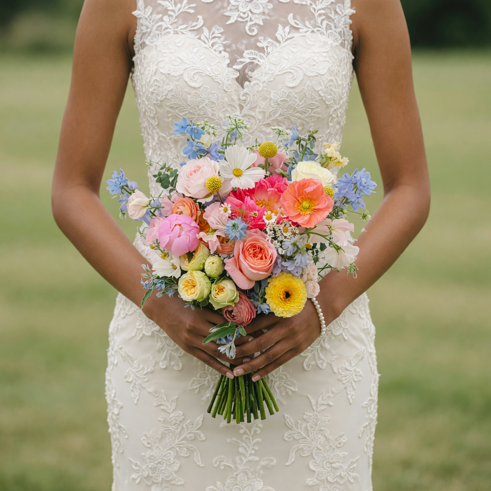 Colorful bouquet for bride with coral garden roses, blush peonies, Iceland poppies, blue delphiniums, white cosmos, chamomile daisies, ranunculus, and seasonal flowers.