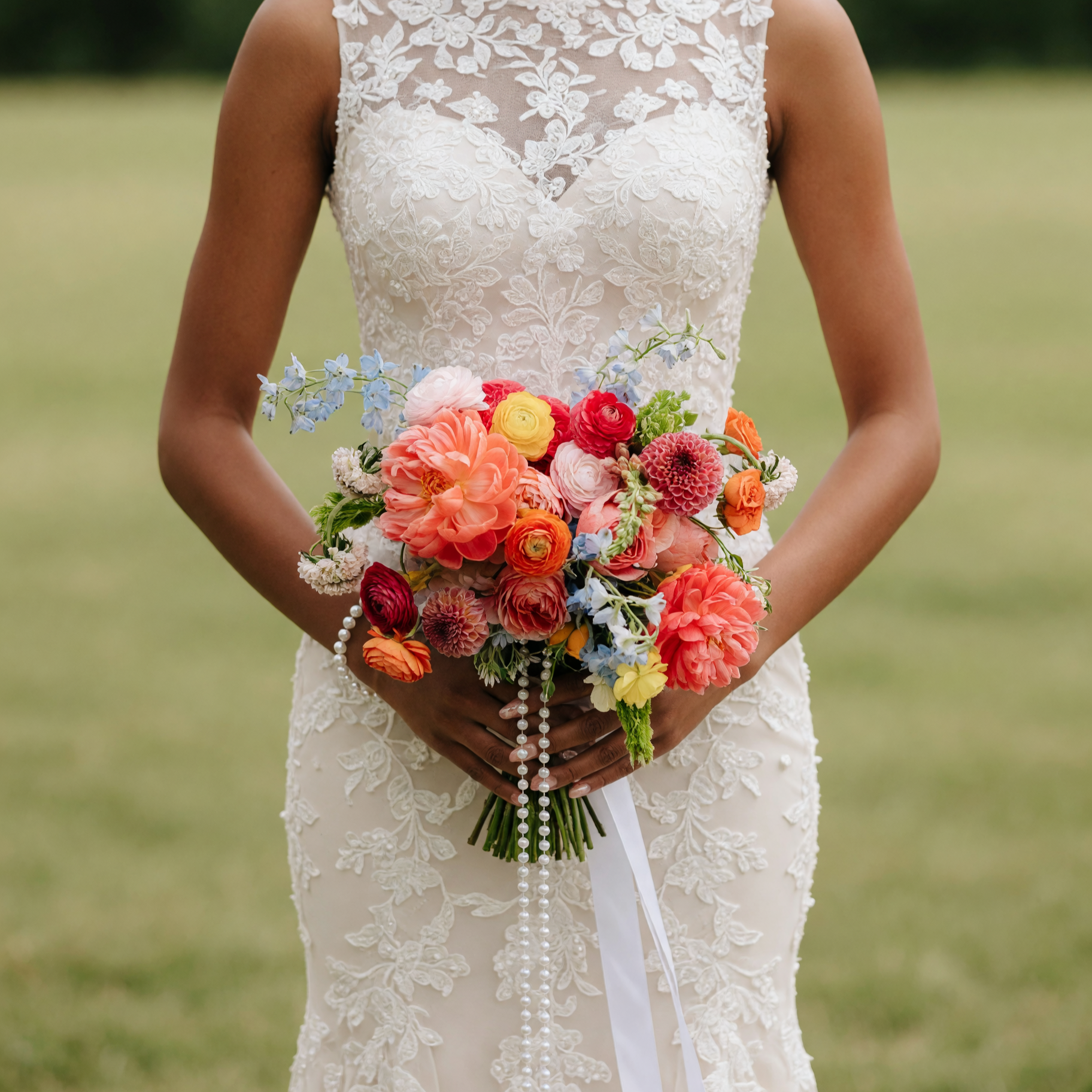 Popular wedding bouquets with coral dahlias, ranunculus, roses, blue delphiniums, seasonal flowers, and elegant pearl strand for brides.