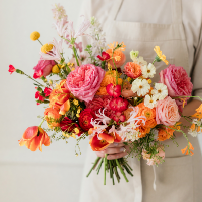 Bridal blooms with pink garden roses, coral and orange flowers, cream blossoms and golden accents in a loose colorful wedding bouquet.