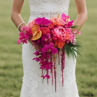 florist styles with fuchsia orchids coral peonies golden anthurium palm leaves and cascading burgundy flowers for a tropical bridal bouquet