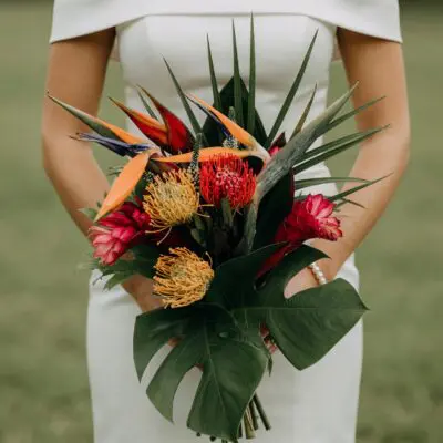 popular wedding bouquets with bird of paradise protea red ginger monstera leaves and dark tropical greenery for a modern bridal look