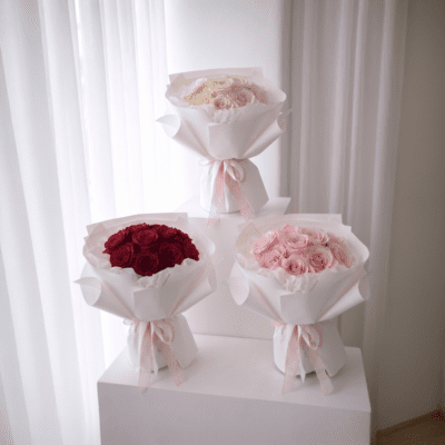 Three bouquets of a dozen roses in red, blush pink, and ivory tones wrapped in white paper with ribbon