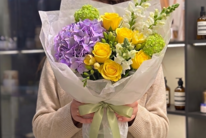 Yellow roses and lavender hydrangea bouquet with green accents wrapped in soft white paper