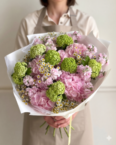 Soft pink hydrangea bouquet with green viburnum and small white daisy flowers wrapped in white paper