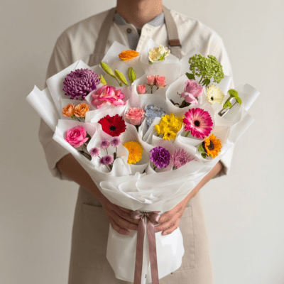 Modern bouquet with individually wrapped colorful flowers including roses, gerbera, and mixed blooms in white paper wrap
