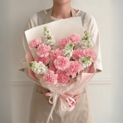Soft pink carnation bouquet with white accent flowers wrapped in blush and white paper with ribbon
