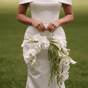 White Wedding Bouquet with cascading white orchids, calla lilies, and trailing greenery, held by a bride in a minimalist off-the-shoulder wedding gown.