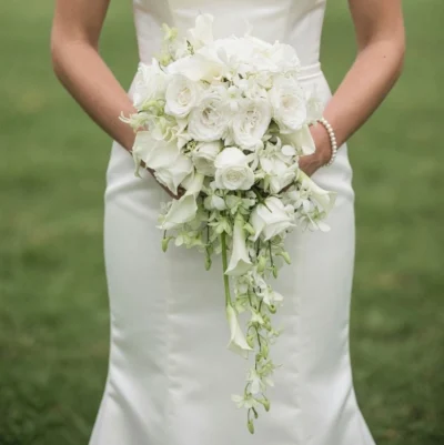 Wedding flowers bridal bouquet featuring white roses, calla lilies, orchids, hydrangeas, and cascading white orchids held by a bride.