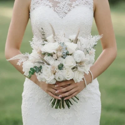 Boho style flowers in a white wedding bouquet with ivory roses, dried palm leaves, eucalyptus, white pompon flowers, and natural grasses.