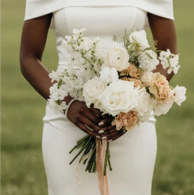 Bridal blooms in a white wedding bouquet with white roses, ranunculus, blush carnations, delphinium, and delicate seasonal flowers.