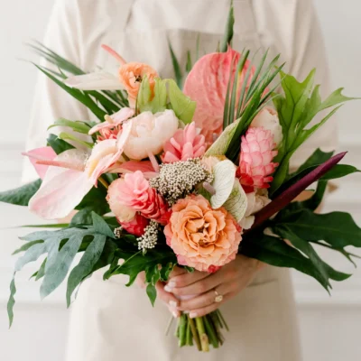 Boho style flowers Coral Paradise Pink Wedding Bouquet with coral roses, blush anthuriums, peonies, pink ginger, monstera leaves, palm foliage, and tropical greenery