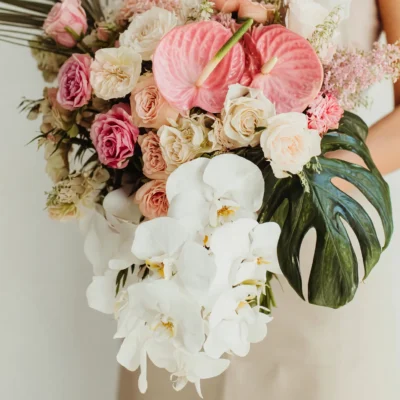 Bridal flowers bouquets with cascading white Phalaenopsis orchids, pink anthuriums, blush roses, tropical monstera leaves, and luxury wedding flowers.