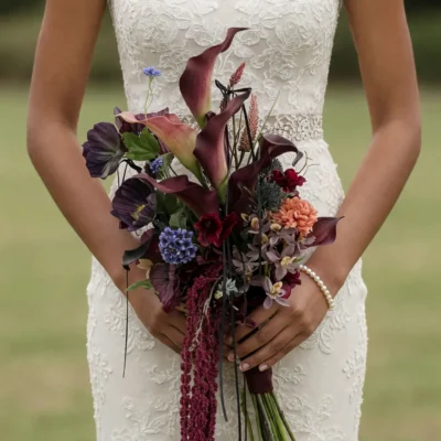 Image Alt Text Boho style flowers bridal bouquet with plum calla lilies, burgundy blooms, orchids, blue flowers, cascading amaranthus, and textured botanicals