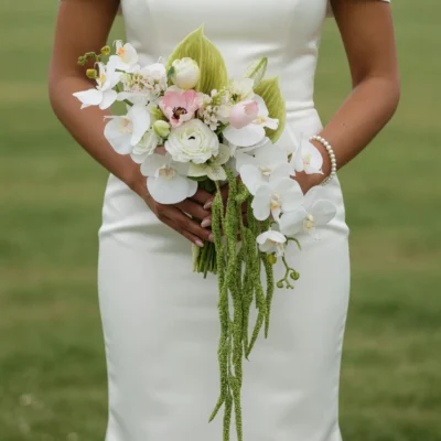 Beach Wedding Bouquets arrangement featuring white phalaenopsis orchids, blush anemone, ranunculus, pale tulip, tropical leaves, and trailing green amaranthus