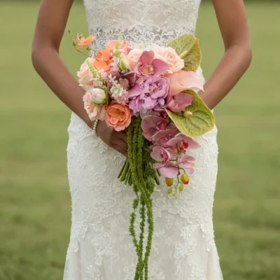 Beach Wedding Bouquets arrangement featuring peach and coral roses, mauve peony, dusty pink orchids, green anthuriums, calla lilies, and trailing amaranthus
