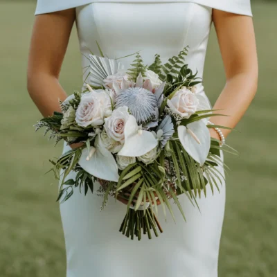 Beach Wedding Bouquets arrangement featuring silver king protea, ivory roses, white anthuriums, hydrangea, metallic palm accents, ferns, and tropical greenery