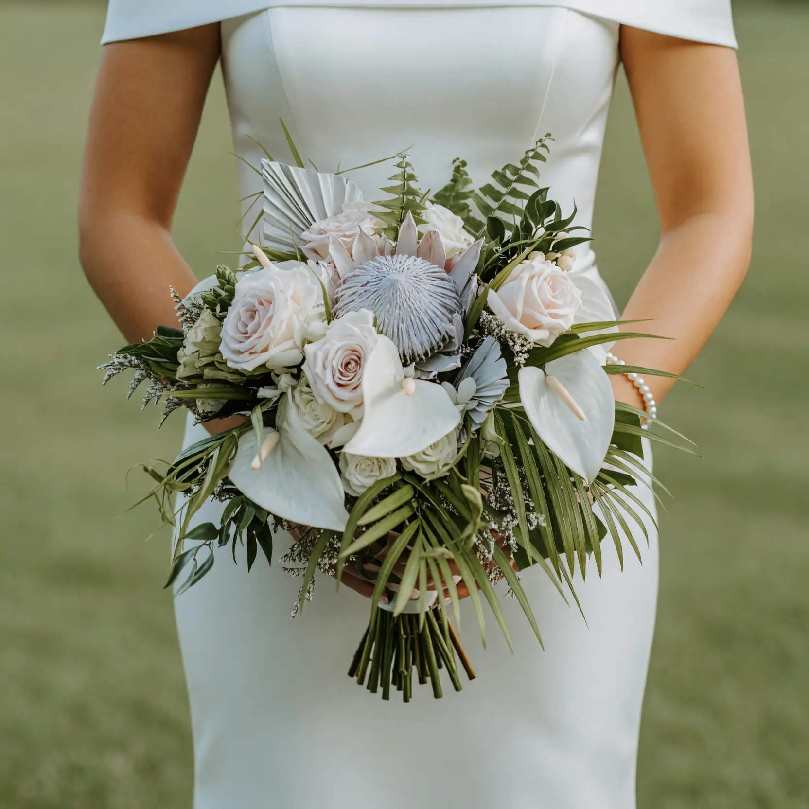Beach Wedding Bouquets arrangement featuring silver king protea, ivory roses, white anthuriums, hydrangea, metallic palm accents, ferns, and tropical greenery