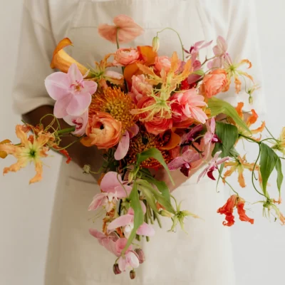 Beach Wedding Bouquets featuring coral and peach roses, pink orchids, orange pincushion protea-like blooms, flame-shaped flowers, and flowing greenery