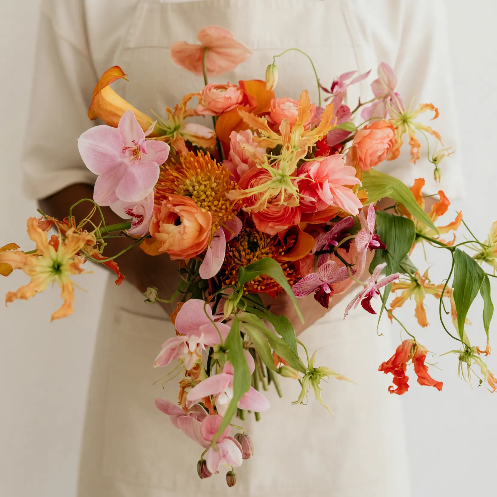 Beach Wedding Bouquets featuring coral and peach roses, pink orchids, orange pincushion protea-like blooms, flame-shaped flowers, and flowing greenery