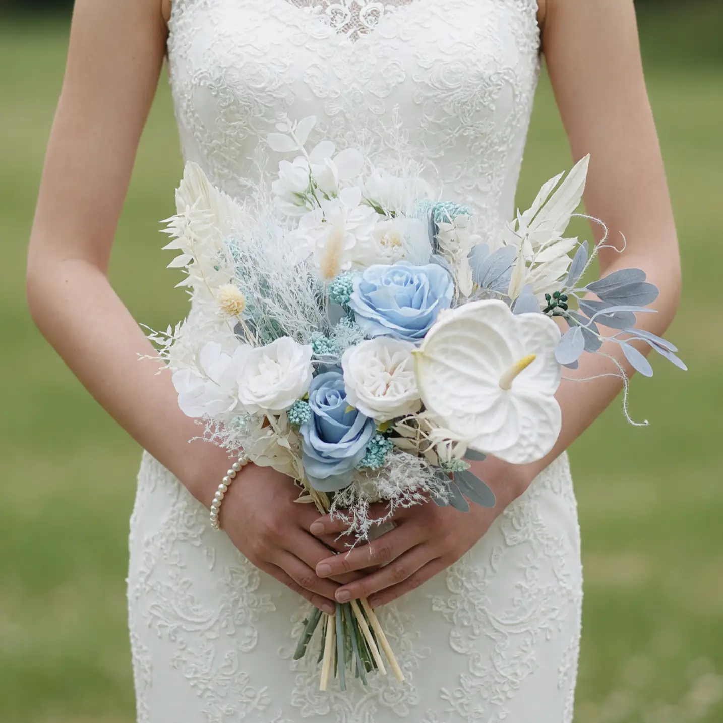 Beach wedding bouquet with powder-blue roses, a white anthurium, ivory flowers, pale silver foliage, and airy dried botanical details.