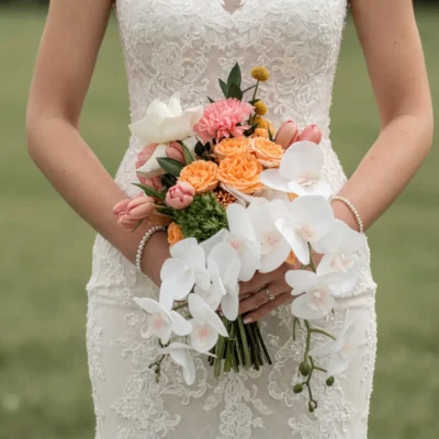 Beach wedding bouquet with peach roses, white cascading orchids, calla lilies, pink tulip-like flowers, and golden button blooms.