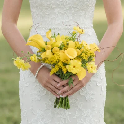 Bride holding a yellow wedding bouquet featuring calla lilies, craspedia-like round blooms, yellow orchid-like flowers, foliage, and curling branches.