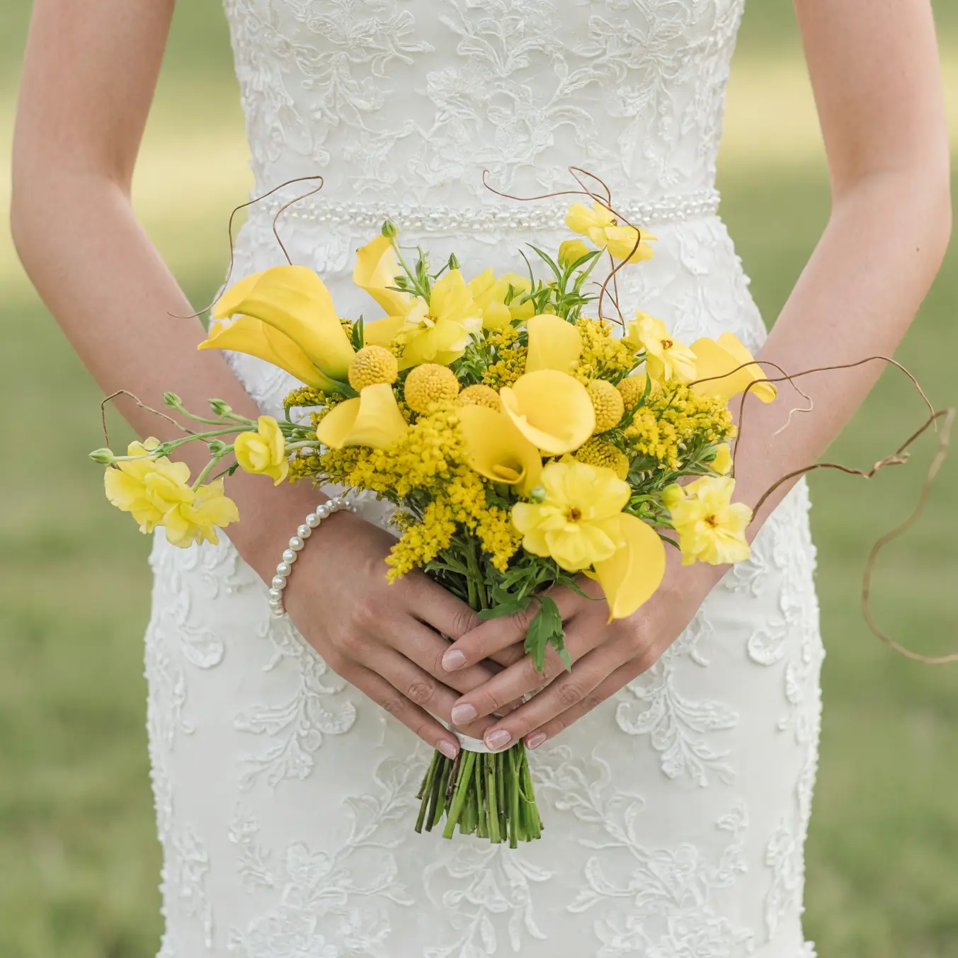 Bride holding a yellow wedding bouquet featuring calla lilies, craspedia-like round blooms, yellow orchid-like flowers, foliage, and curling branches.