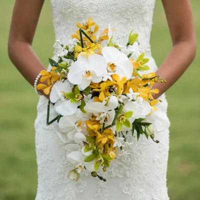Yellow and white cascading wedding bouquet of orchids, green cymbidiums, white blossoms, and blue accents held by a bride