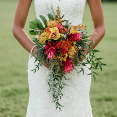 Boho style flowers in a cascading wedding bouquet with tropical orchids, protea, lush greenery, and vibrant bridal blooms.