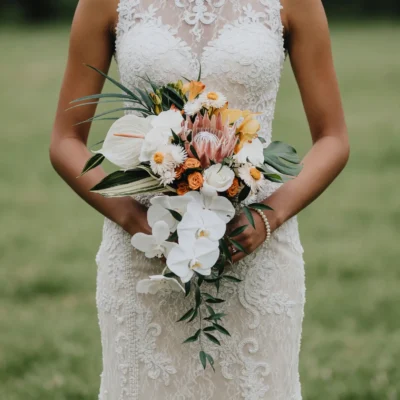 Boho style flowers with cascading white orchids, king protea, golden roses, chamomile flowers, tropical foliage, and elegant bridal bouquet.