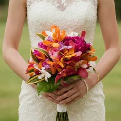 Bridal flowers bouquets with orange orchids, pink roses, magenta tropical blooms, white orchids and glossy greenery for a vibrant wedding.