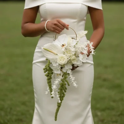 Bridal flowers bouquets featuring ivory white blooms, layered floral textures, cascading green botanical accents, and a circular gold handle held by a bride.