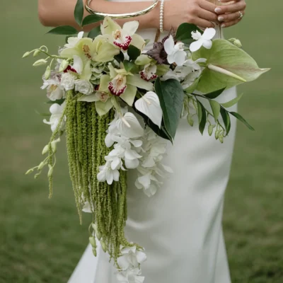 Bridal flowers bouquets with ivory and pale green orchid-like blooms, white flowers, dark green foliage, cascading botanical textures, and a modern wedding gown.