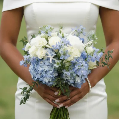 bridal blooms with creamy white roses pale blue hydrangeas delicate blue flowers and fresh greenery held by a bride in a white wedding dress