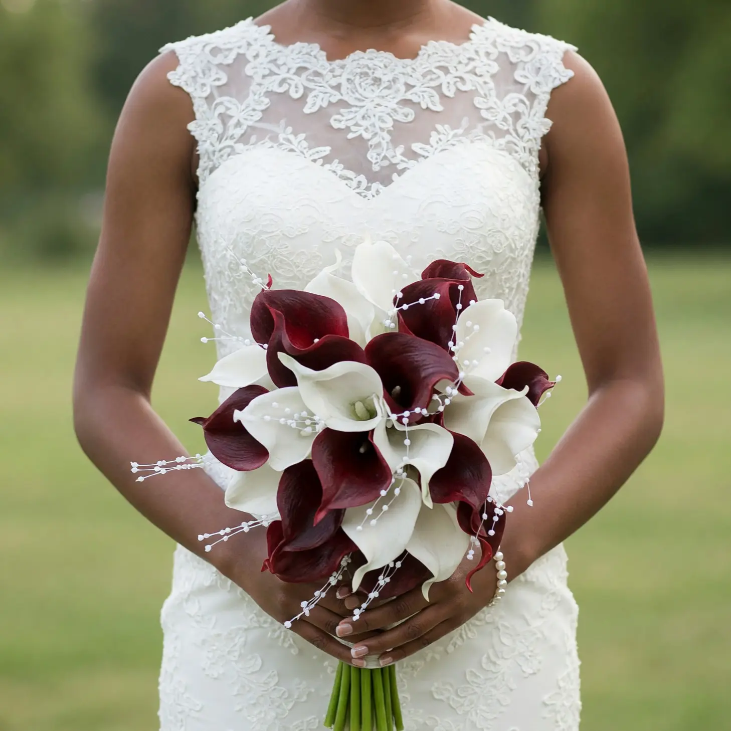 Bride holding a burgundy and ivory calla lily wedding bouquet with delicate white beadlike floral accents against a detailed lace wedding dress.
