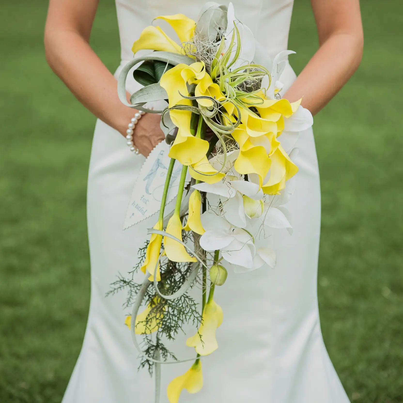 Yellow calla lily bridal bouquet with white orchids, curled foliage, trailing greenery, and a dramatic cascading design