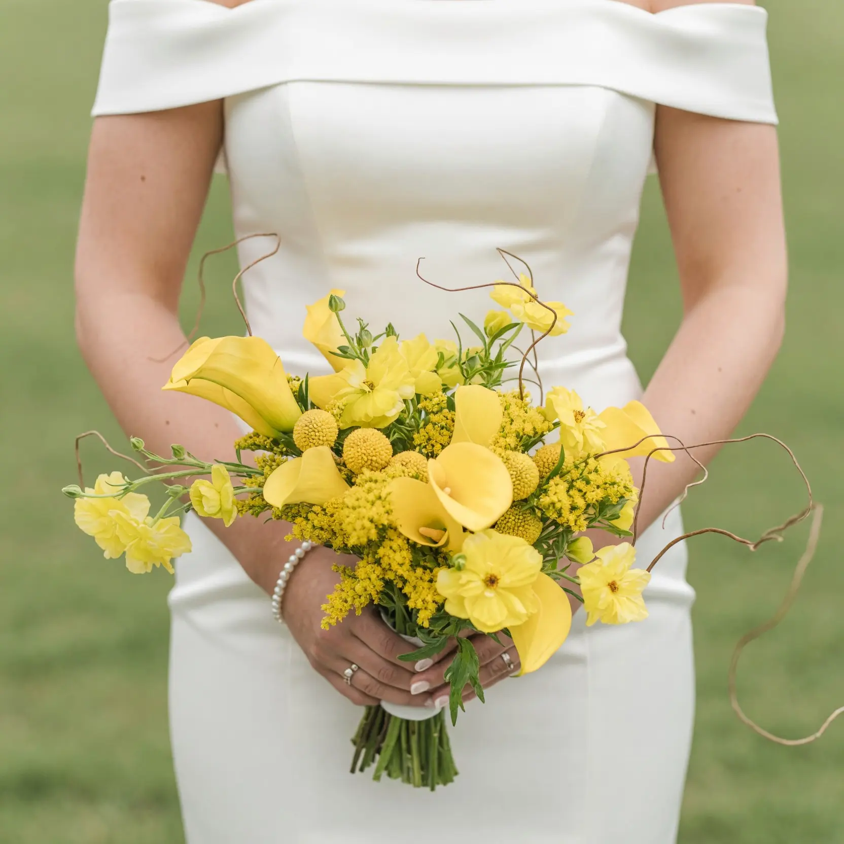 Yellow wedding bouquet with calla lilies, billy balls, golden wildflowers, greenery, and curling branches held by a bride